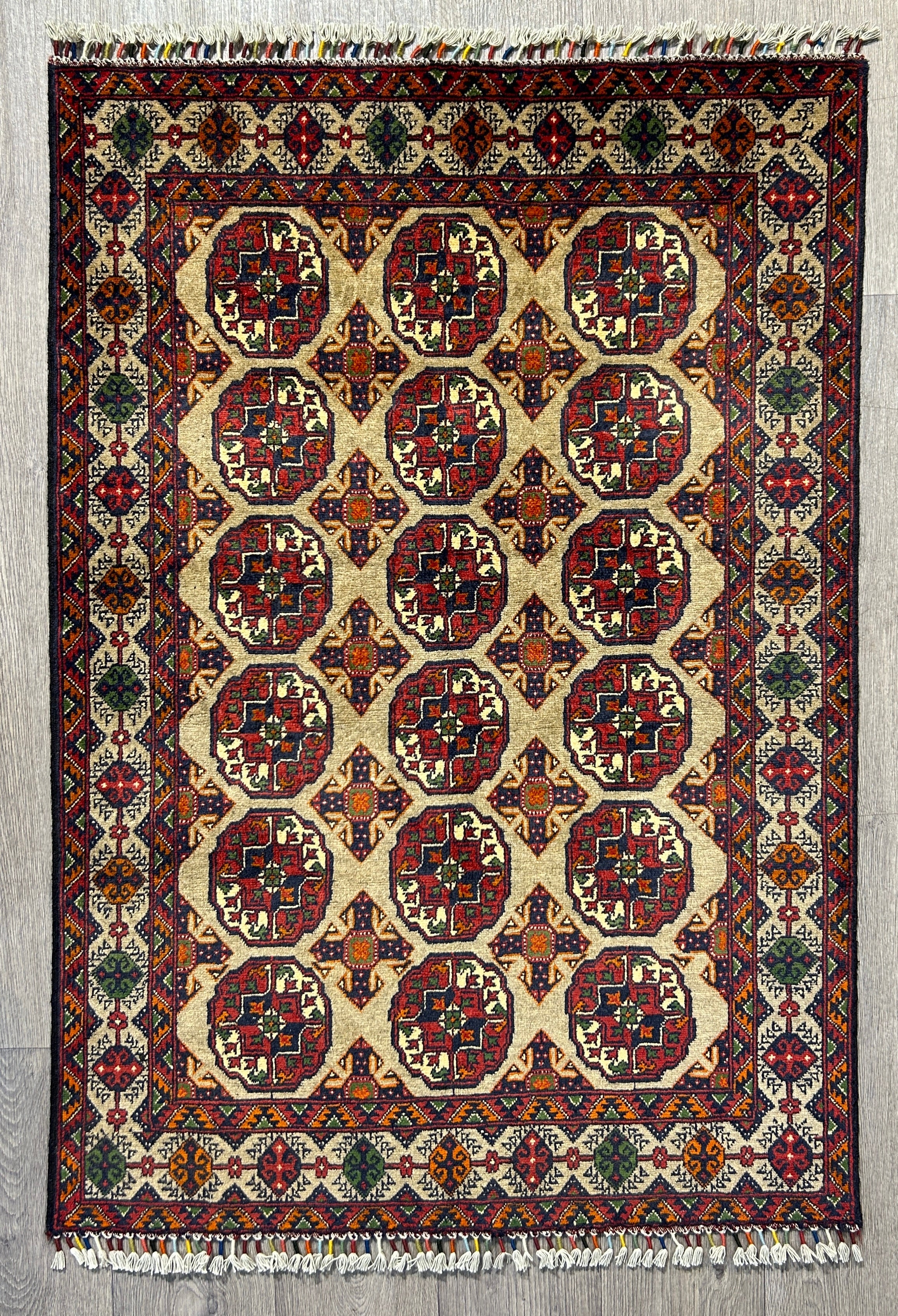 Authentic Handknotted Beige Afghan Kundus Wool Rug 139cm x 96cm
Traditional elephant foot gul motifs in multiple veg dyed colours including red blue and orange.  The rug has a heraldic feel to it.The rug features a soft background in a natural shade of sheep's wool