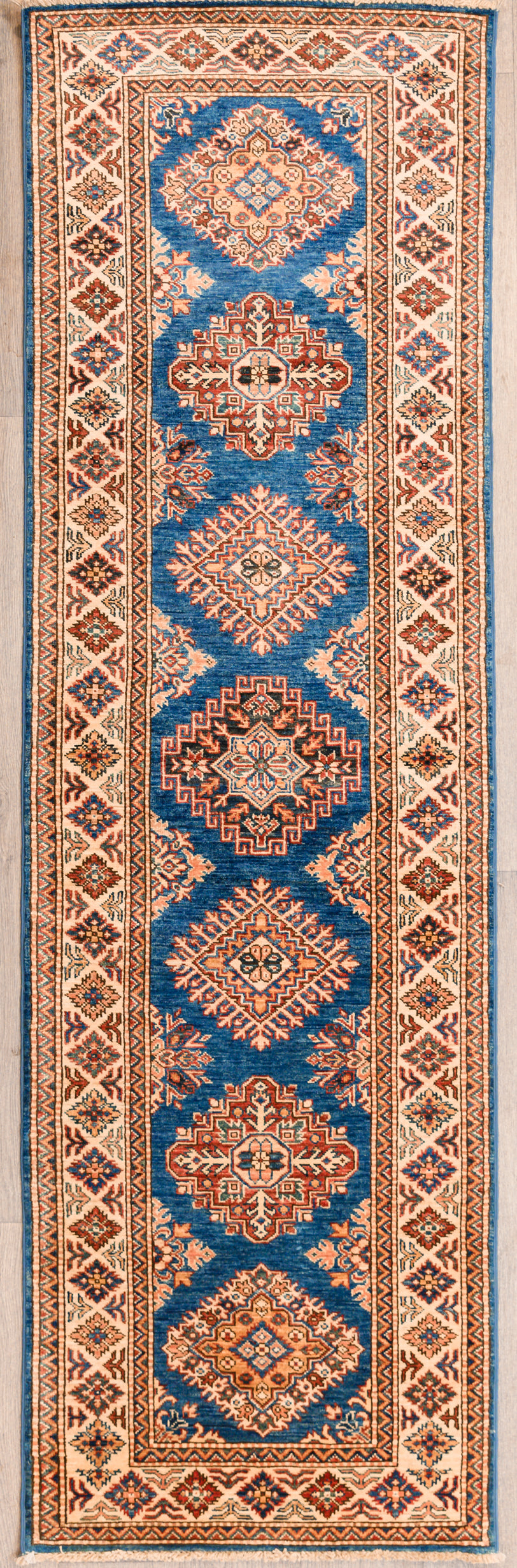 Authentic Hand Woven Blue Afghan Super Kazak Wool Runner 256cm x 77cm
Beautiful blue &amp; cream tones all over made from local vegetable &amp; plant dyes

Woven Using Premium Quality Wool gives an Unrivallled Shine Off the Pile
Originating from the Caucaus Region, the Kazak Design is now Mastered by the Generational Weavers of North-Central Asia